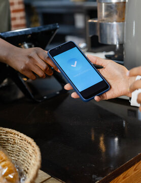 Smartphone showing blue checkmark is being exchanged at cafe counter with pastry basket nearby