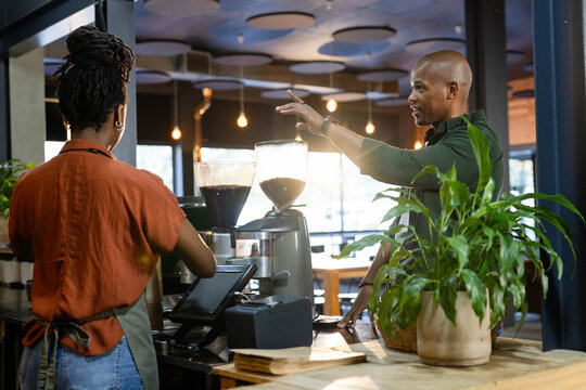 African American barista in apron and customer talking using espresso machine and grinders at cafe