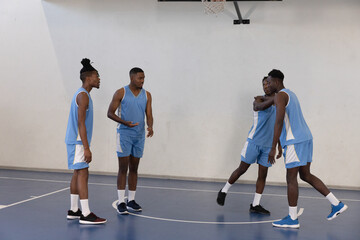 African American male team standing on court in gym wearing light-blue jerseys embracing under hoop