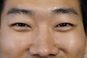 Asian man holding narrow-eyed gaze in studio close-up, showing pores and light stubble