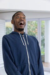 African American adult man standing in navy hoodie by glass doors and column, showing astonishment