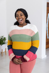 African American woman laughing in home entry wearing striped sweater with plant and wooden door