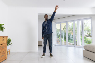 African American man in 20s standing in living area reaching upward toward glass doors
