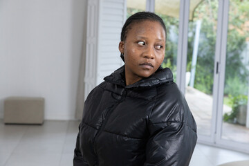 African American woman standing by sliding glass doors, looking right, wearing black puffer jacket