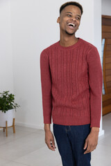 African American man laughing near doorway at home wearing red knit sweater beside potted plant