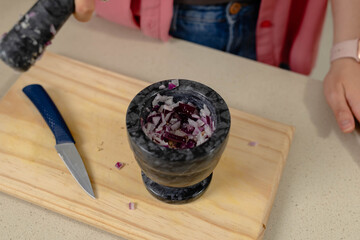 Black marble mortar holding chopped red onion on wooden cutting board, blue-handled knife resting
