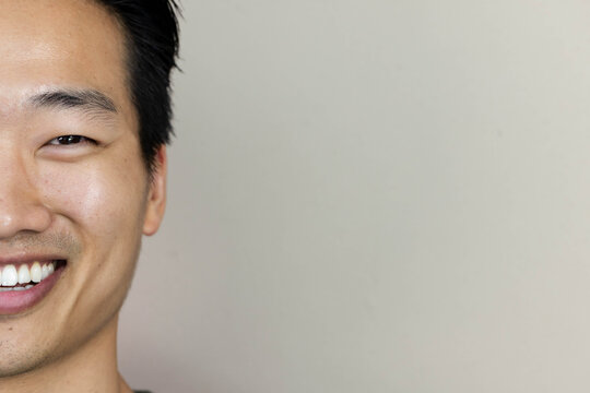 Left half of man's face is filling frame against pale gray-beige wall, showing smile, copy space