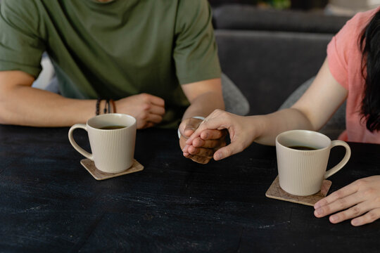 Couple holding hands across textured table in lounge, green and pink tops, ribbed mugs, bracelet