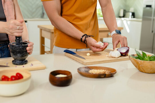 Diverse couple cooking at modern kitchen island, man in orange Tshirt peeling garlic on board