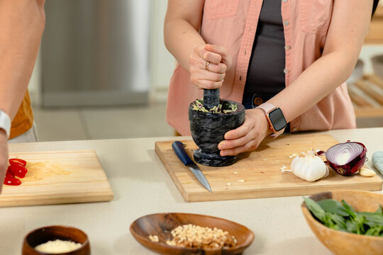 Asian couple preparing ingredients in home kitchen, female crushing garlic with mortar and pestle