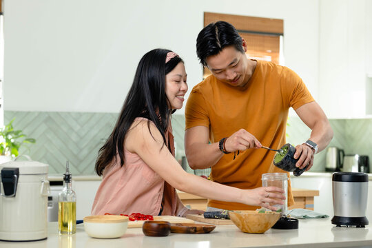 Asian couple preparing meal at central kitchen counter, scooping green paste into glass jar