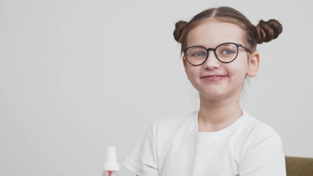 Child with glasses sprays liquid medicine into her mouth while seated indoors. Concept child health, medication intake, pediatric treatment