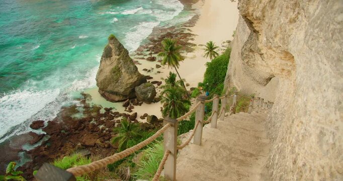 White waves crash against the rocky shore below the steep cliff path at Diamond Beach Nusa Penida Bali