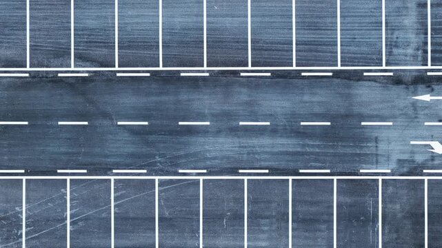Aerial shot of an empty asphalt parking lot with white lines in a generic urban area during the day.