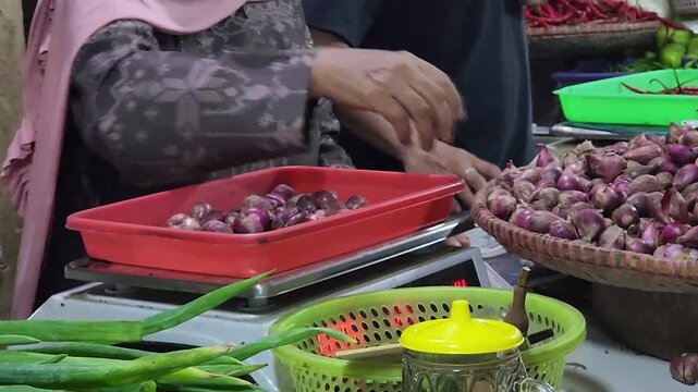 Vendor weighing red onions on scale at traditional vegetable market. Market seller measuring shallots for retail purchase and packaging. Hands sorting and weighing red onions