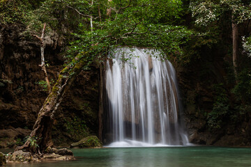Erawan Falls cascading through lush forest in Erawan National Park. Tropical greenery surrounds the flowing waterfall. Located in Kanchanaburi, Thailand, a serene natural landscape.