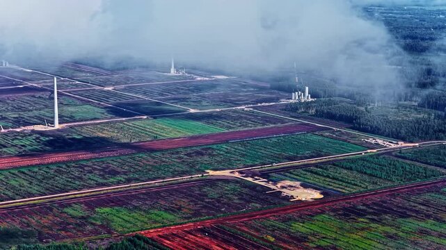 Drone shot of massive renewable energy project in Latvia showing installed wind turbine towers and active heavy-duty cranes at a construction site in the rural landscape.