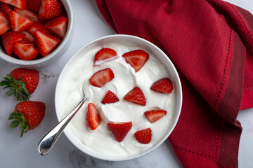 A bowl of creamy Greek yogurt fresh sliced strawberries, photographed in natural light on a marble surface. Styled as a healthy breakfast or snack with clean, minimal composition and vibrant color con