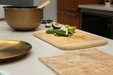 A bright kitchen scene featuring fresh ingredients prepared on a wooden cutting board, including avocado and cucumber, ready for a healthy meal preparation on the kitchen table.