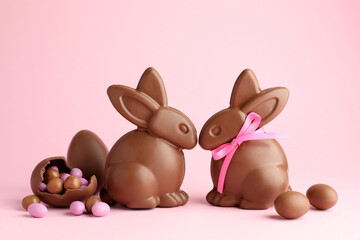 Chocolate Easter bunnies and eggs with candies on pink background