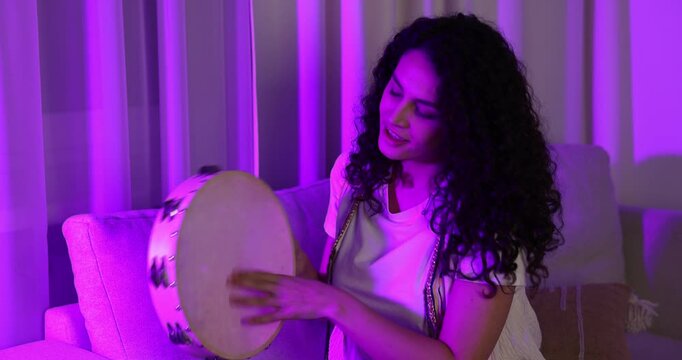 Woman playing tambourine in pink light at home