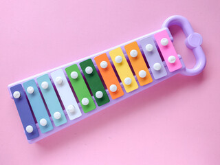 Toy xylophone made of metal and plastic (glockenspiel). A xylophone with colorful keys. The xylophone is placed on a pink background
