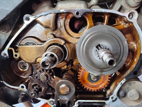 Close-up of an open motorcycle engine crankcase showing internal gears, shafts, and mechanical components covered in engine oil during repair or maintenance in a workshop.