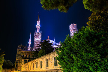 Naklejka premium Night view of a majestic illuminated mosque with minarets and lush greenery