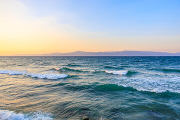 Obraz premium Tranquil sunset on the mediterranean sea with gentle waves and distant mountains