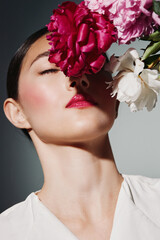 Fashion model with flawless glowing skin and shiny red lips poses with face partially covered by...