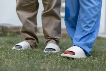 Close-up of senior man and nurse walking together on grass, showing supportive steps in rehabilitation, elderly mobility care. Concept of physical therapy, recovery, home healthcare services.