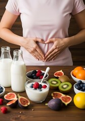 Healthy woman making heart gesture over stomach with yogurt milk and fresh fruits on wooden table