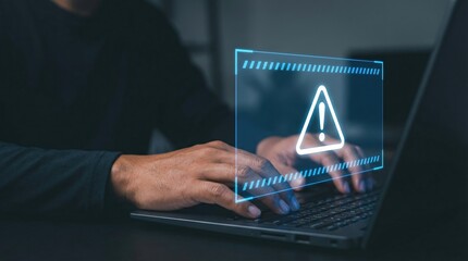 Person typing on laptop in dim light with glowing digital warning sign for online security alert