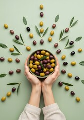 Top view flat lay of hands holding a bowl with fresh mixed olives and leaves on green background