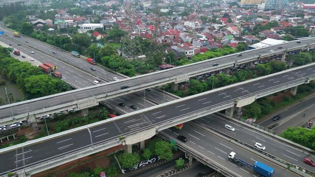 Aerial view of busy toll road crossing dense city area with bridges, cars, and urban housing, showing transport flow and city growth.