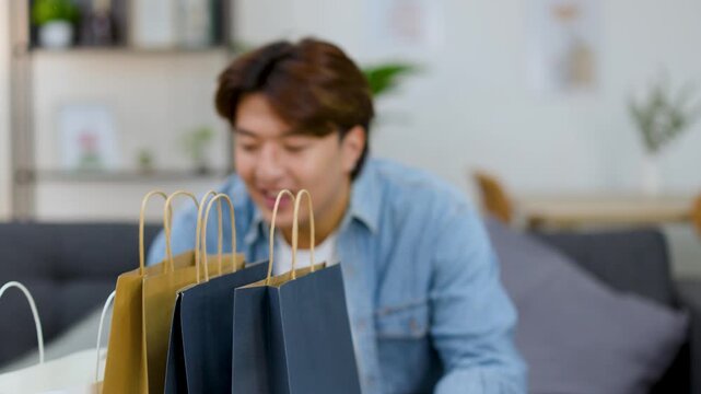 Excited Asian Man Unpacking New Clothes From Shopping Bags at Home