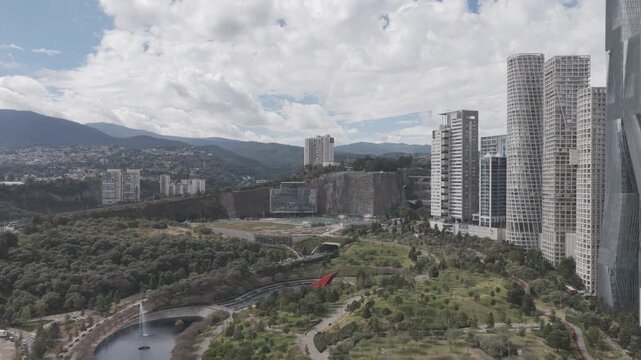Aerial drone flying backwards over Parque La Mexicana with skyscrapers, mountains and cloudy sky in Santa Fe, M&eacute;xico City. Shot in D-Log M
