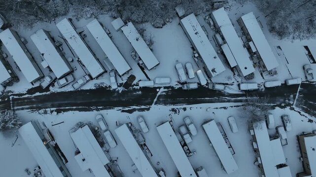 Snow-covered residential neighborhood with parallel housing rows, parked cars and narrow road. Geometric winter patterns in quiet American community. Mobile trailer homes in America.