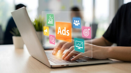Person typing on laptop with digital advertising and marketing icons overlay in a bright modern offi