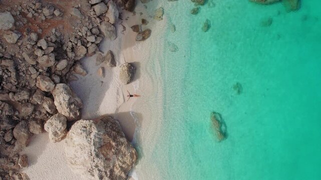 Remote Kefalonia cove with woman resting on sand between rugged rocks and turquoise sea in Greece