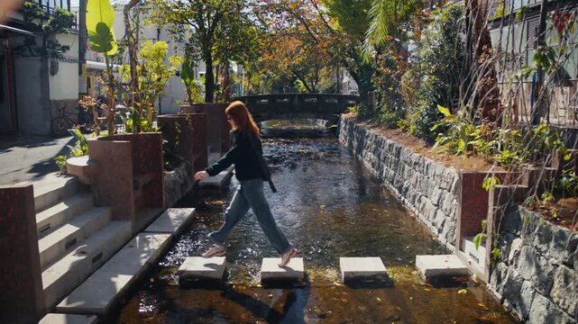 Woman crossing an urban canal on stepping stones in a beautiful park