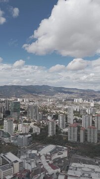 Aerial drone flying sideways over Centro Comercial Santa Fe with urban density, mountains and cloudy sky in M&eacute;xico City. Vertical video