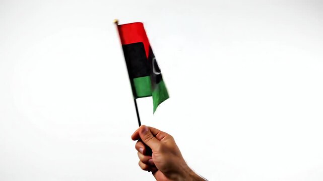 Hand holding Libyan flag waving in the wind against white background
