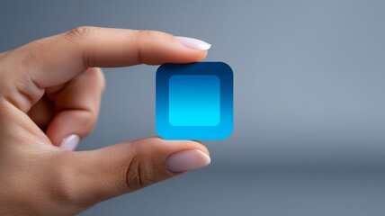Female hand holding a small transparent blue square on gray background