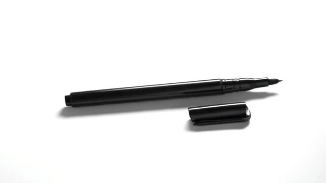This video segment captures a close-up, high-angle view of a sleek black marker pen resting on a pristine white background, its matching cap neatly placed alongside. The sharp contrast between the dar