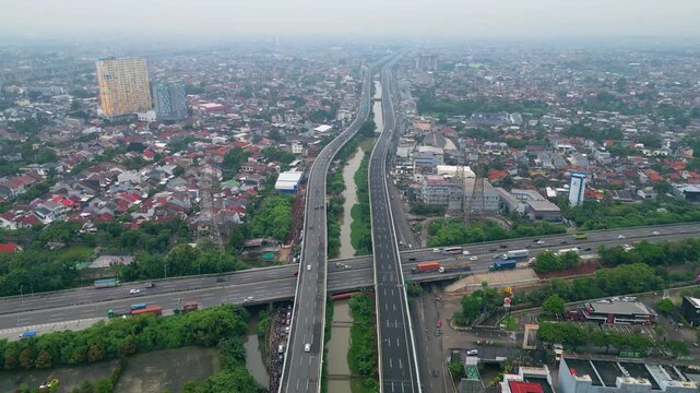 Aerial view of busy toll road crossing dense city area with bridges, cars, and urban housing, showing transport flow and city growth.