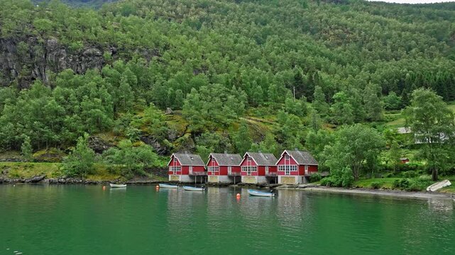Traditional red boathouses reflected in the fjord near Fl&aring;m, Norway. Scenic Norwegian coastal village with calm water and lush forest highlights quiet rural life and nature.