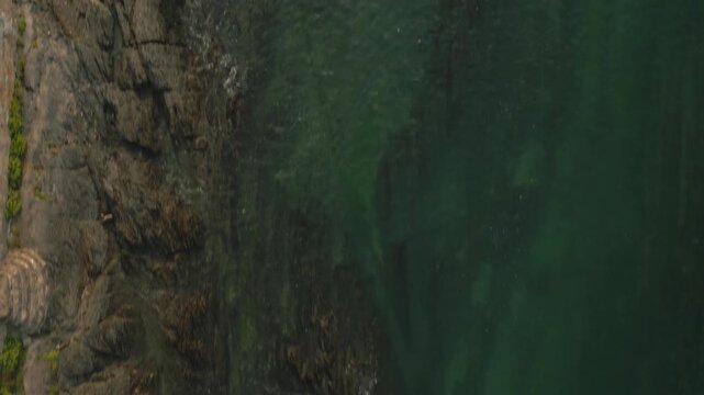 An aerial view shows a rocky coastline meeting dark green water.