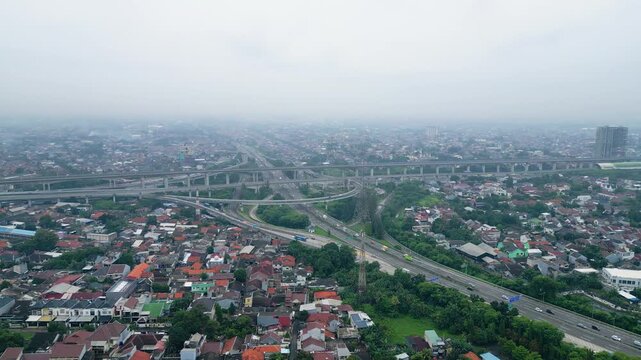 Aerial view of busy toll road crossing dense city area with bridges, cars, and urban housing, showing transport flow and city growth.