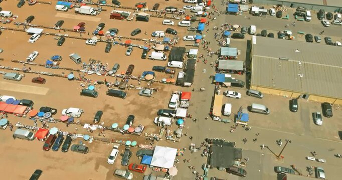 Many people walk between cars in large open air flea market filled with tents tables. It is area shows busy activity various vendors.